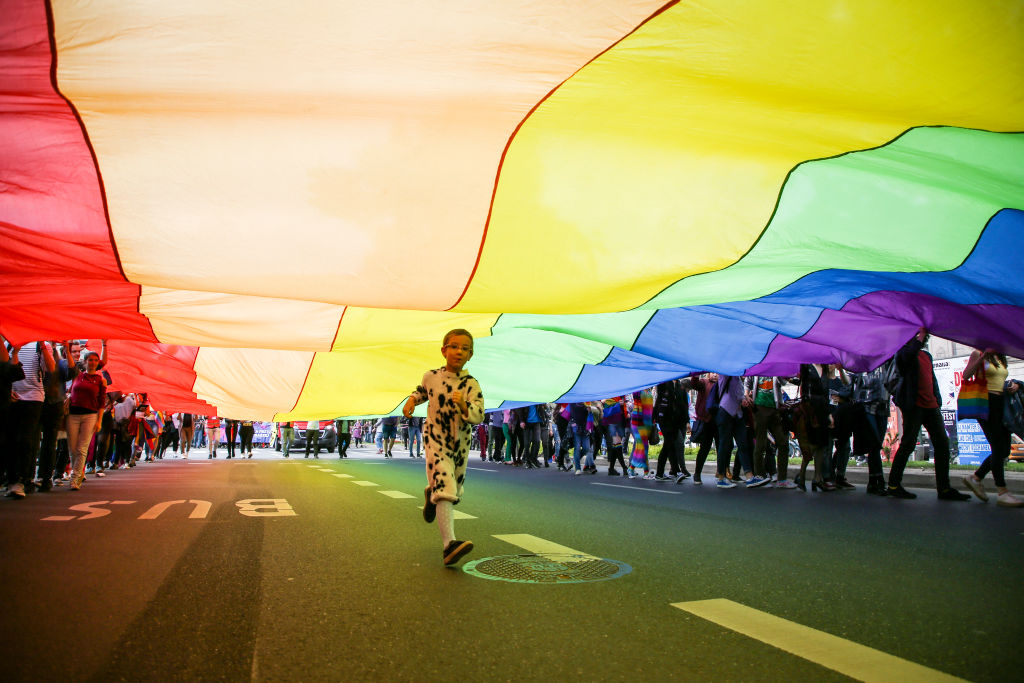 Child runs on the street with a massive Pride flag over him, during an Equality March in Krakow, Poland.