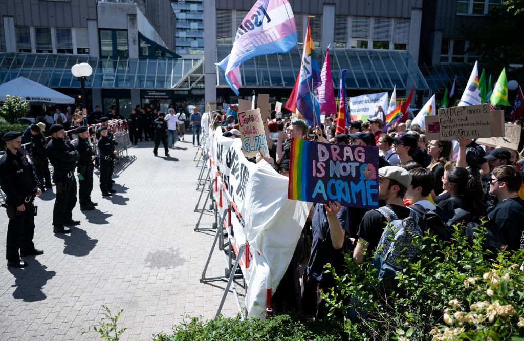 Participants of a solidarity demonstration (r) stand under the motto "Munich is colorful" in front of the district library and behind police barriers before the reading begins. Under the motto "We read you the world as you like it" drag queens read books to children in a district library.