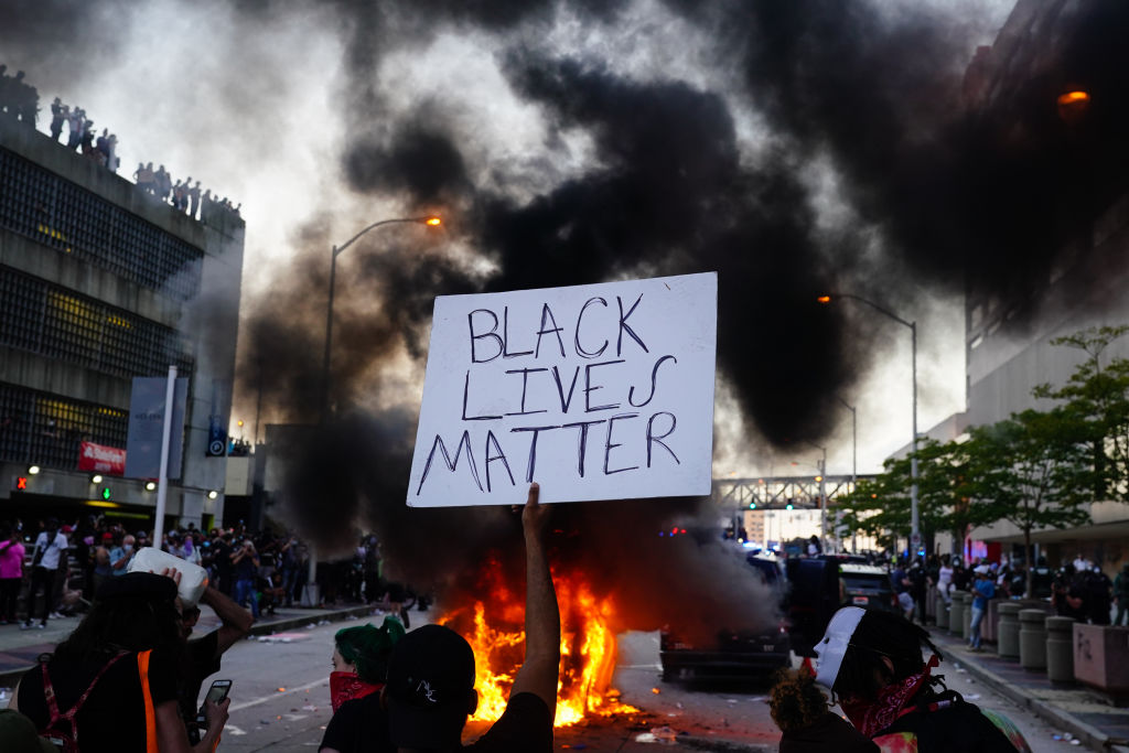 A man holds a Black Lives Matter sign as a police car burns during a protest on May 29, 2020 in Atlanta, Georgia.