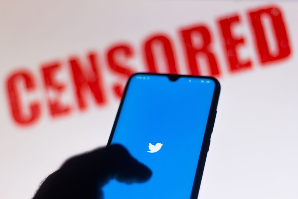 Twitter logo is displayed on a smartphone and a red alerting word "CENSORED" on the blurred background.