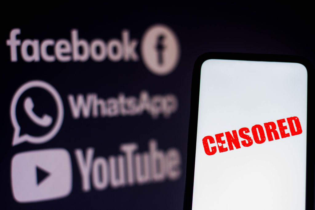 The word 'censored' is seen displayed on a smartphone with the logos of social networks Facebook, WhatsApp and YouTube in the background.