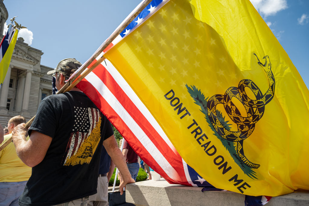 A man with a Gadsden flag, a US flag, and a Confederate battle flag listens to a speaker during the Kentucky Freedom Rally at the capitol building on August 28, 2021 in Frankfort, Kentucky.