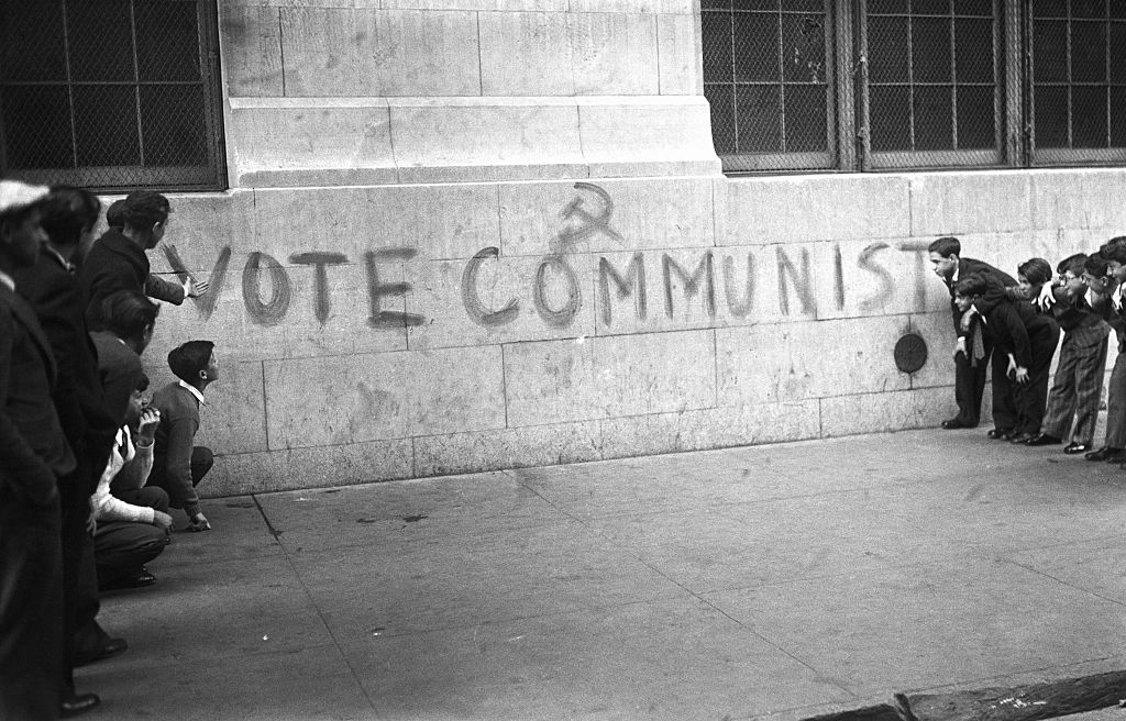 New York, NY: Although it was probably meant for their elders, this specimen of Communist propaganda is being examined by a few school children from the public school at 114th Street and 3rd Avenue, on the walls of which it is painted. Emblem above the sign makes it official.