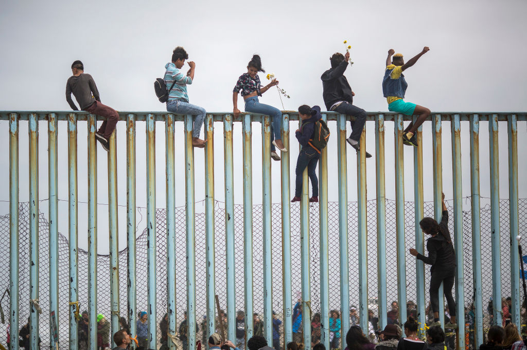 People climb a section of border fence to look toward supporters in the U.S. as members of a caravan of Central American asylum seekers arrive to a rally on April 29, 2018 in Tijuana, Baja California Norte, Mexico.