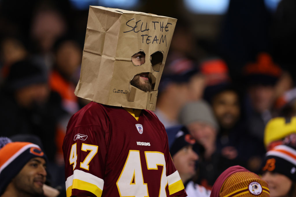 A Washington Commanders fan looks on while wearing a sign that reads "Sell The Team" during the second quarter between the Chicago Bears and the Washington Commanders at Soldier Field on October 13, 2022 in Chicago, Illinois.